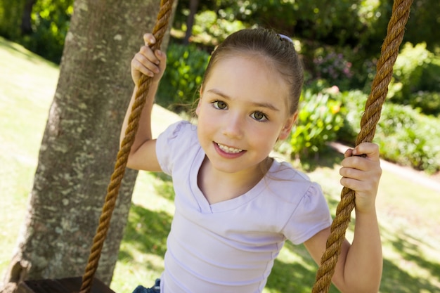 Feliz niña sentada en el columpio en el parque