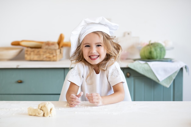 Feliz niña con sombrero de chef en la cocina