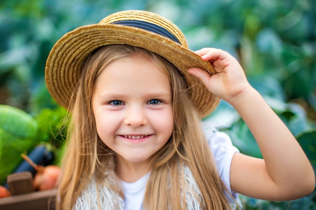 Feliz niña con sombrero de paja en campo de repollo