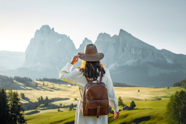 Feliz niña con sombrero de vestido blanco y mochila en Alpe di Siusi Dolomites