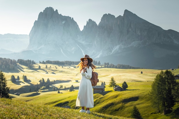 Foto feliz niña con sombrero de vestido blanco y mochila en alpe di siusi dolomites