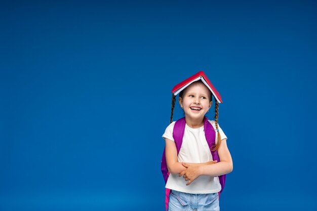 Feliz niña sonriente se divierte en azul con el libro en la cabeza