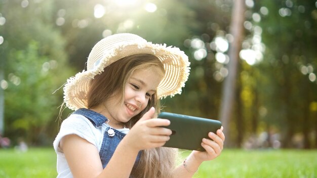 Feliz niña sonriente niño mirando en su teléfono móvil al aire libre en verano.