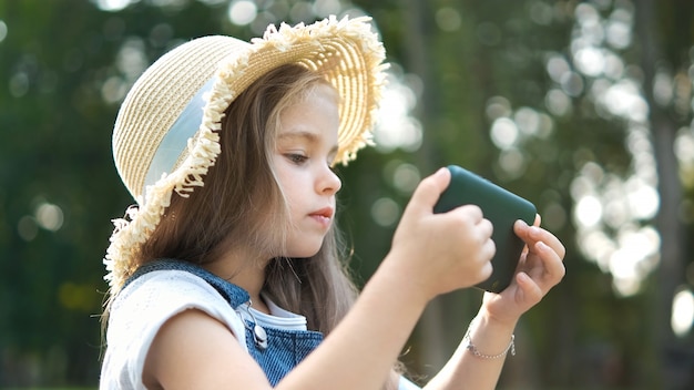 Feliz niña sonriente niño mirando en su teléfono móvil al aire libre en verano.