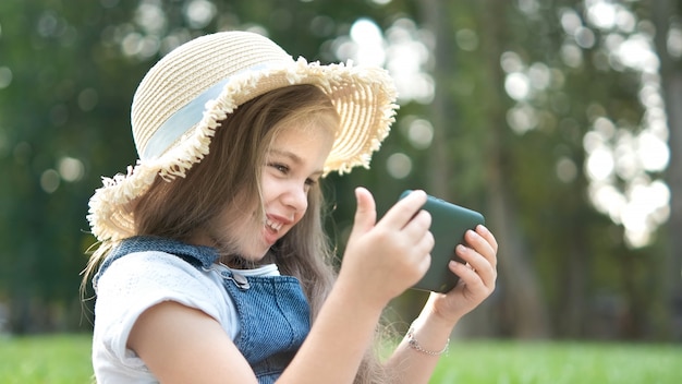 Feliz niña sonriente niño mirando en el teléfono móvil al aire libre en verano.