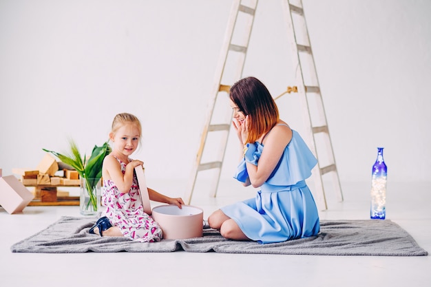 Feliz niña sonriente con su madre desempaqueta un regalo. Hermosa madre con su hija en la habitación decorada en blanco.