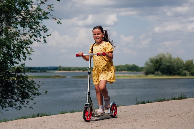 Feliz niña sonriente con un vestido amarillo montando una scooter la niña pasa un buen rato y disfruta de una familia con ...