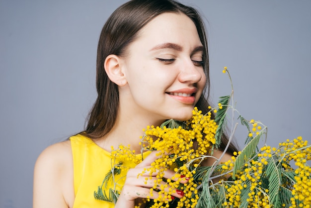 Feliz niña sonriente con un vestido amarillo que huele una mimosa amarilla fragante