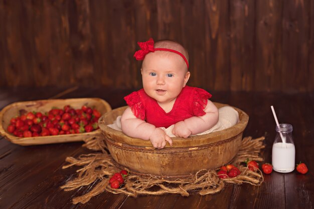 Feliz niña sonriente en un vestido rojo se encuentra boca abajo y come fresas y bebe leche