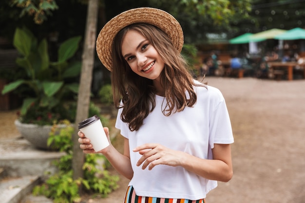 Feliz niña sosteniendo la taza de café para llevar mientras está de pie en el parque al aire libre