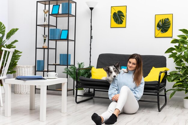 Foto la feliz niñera del perro está sentada en el suelo de la sala de estar y el perro está tendido en el