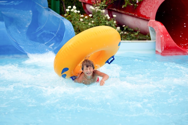 Feliz, un niño de 8 años está montando en el parque acuático en círculos inflables en toboganes de agua con salpicaduras