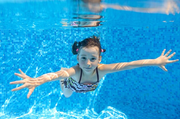 Feliz niño activo nada bajo el agua en la piscina