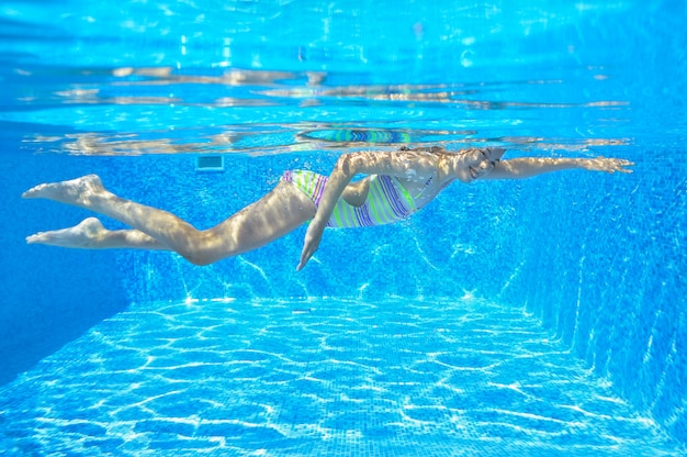 Feliz niño activo nada bajo el agua en la piscina