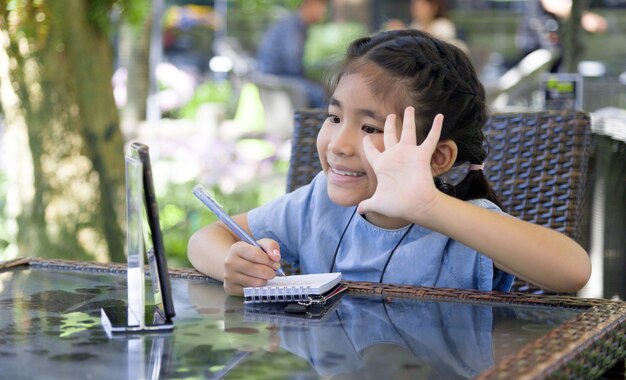 Feliz niño asiático saludando reunión en línea en la aplicación de aula móvil en la pandemia de coronavirus en casa