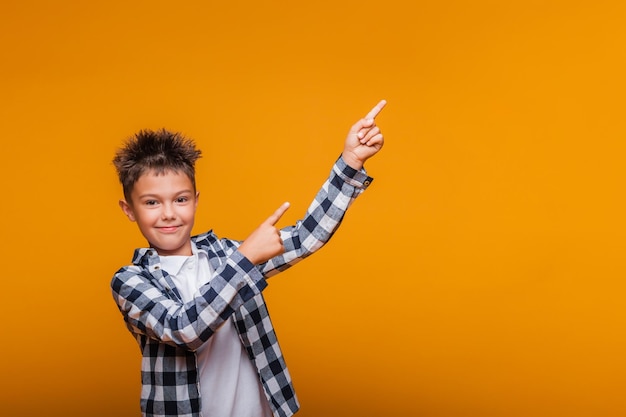 Foto feliz niño emocional sorprendido muestra algo con su dedo sobre fondo azul.