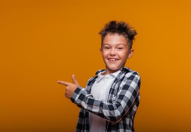 Feliz niño emocional sorprendido muestra algo con su dedo sobre fondo azul.