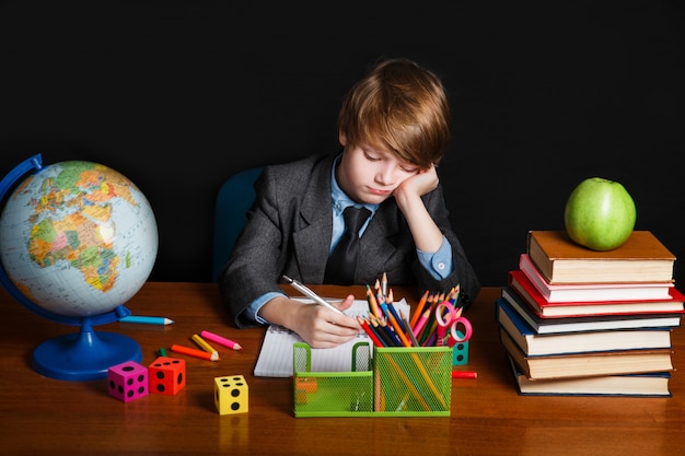 Feliz niño inteligente lindo está sentado en un escritorio en unas gafas y sonriendo.