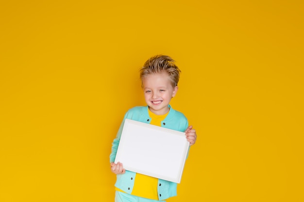 Feliz niño lindo 5-6 años tiene una hoja de papel blanco en blanco en un marco de luz.