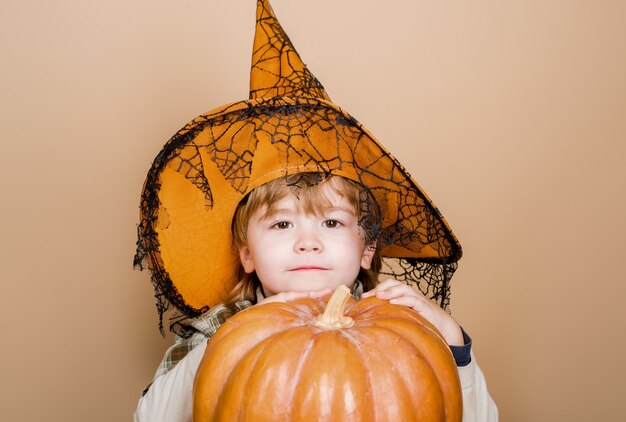 Feliz niño lindo de halloween con sombrero de bruja abrazando calabaza de halloween jack o lantern truco o trato