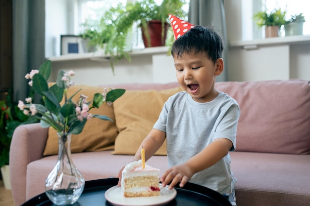 Feliz niño lindo mirando un trozo de sabroso pastel de cumpleaños