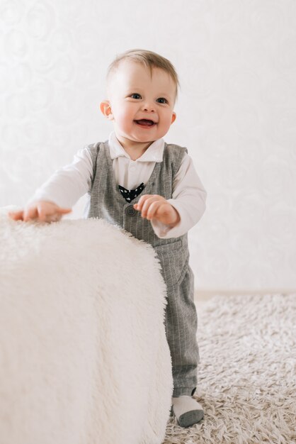 Feliz niño lindo en traje de caballero se encuentra cerca del soporte sobre un fondo claro