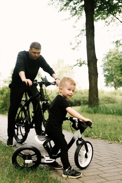 Feliz niño monta una bicicleta con un joven papá en el parque