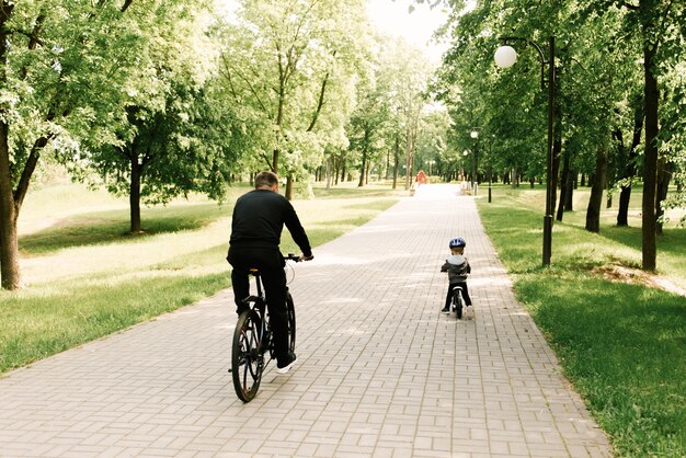 Feliz niño montando una bicicleta con su papá en el parque