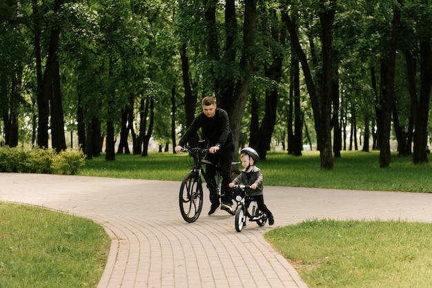 Feliz niño montando una bicicleta con su papá en el parque