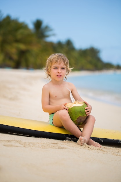 Feliz niño pequeño niño preescolar divertido beber jugo de coco en la playa del océano.