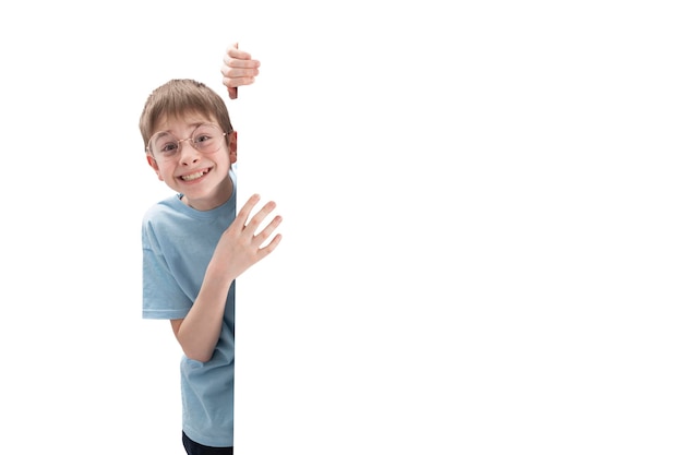 Feliz niño preadolescente sonriente se asoma desde detrás de la pizarra con un espacio en blanco vacío para su texto o anuncio Copiar espacio Aislar