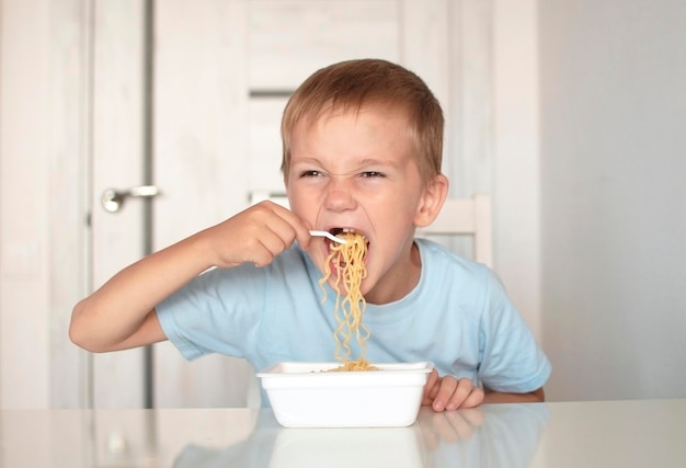 Feliz niño preescolar come pasta espagueti Niño en la cocina en la mesa comiendo fideos Concepto de comida para bebés Disfrute de su comida