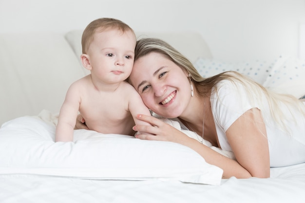 Feliz niño sonriente y madre acostada sobre la almohada y mirando a la cámara