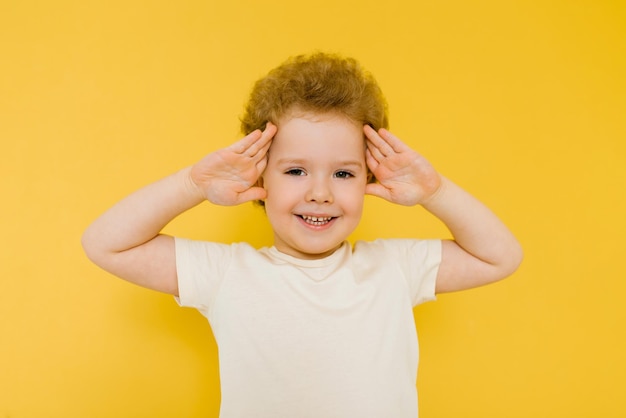 Feliz niño sorprendido sonríe y sostiene sus manos sobre su cabeza sobre un fondo amarillo