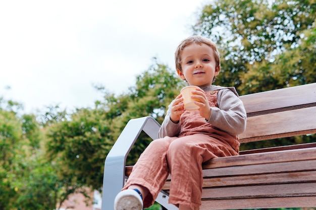 Feliz niño de tres años en la calle sosteniendo una tina de helado sentado en un banco