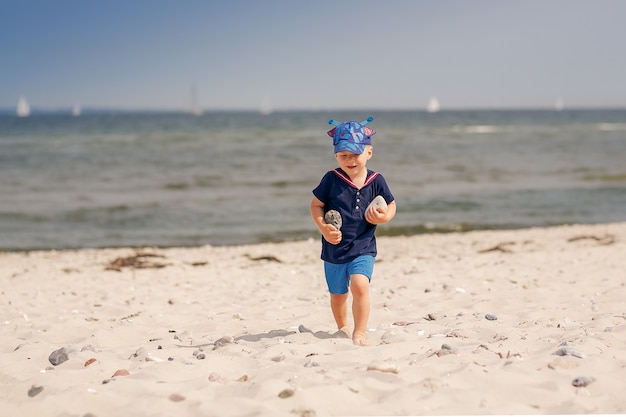 Feliz niño de tres años va a la playa del mar y sostiene piedras en las manos