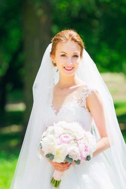 Feliz novia joven en un delicado vestido de novia blanco y velo en