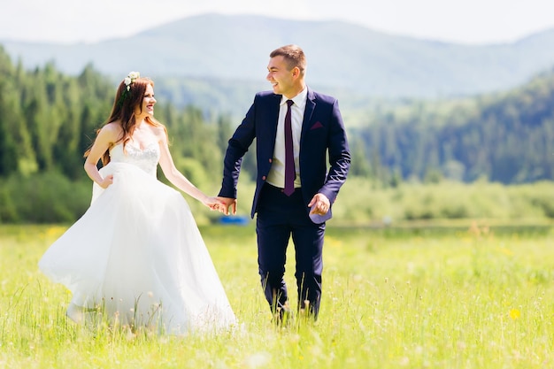 Feliz novia y el novio caminando corriendo y bailando en un prado de verano