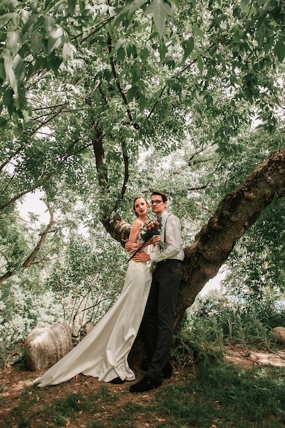 Feliz novia y novio de pie cerca del árbol