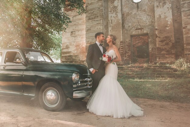 Foto feliz novia y el novio de pie cerca de coches antiguos