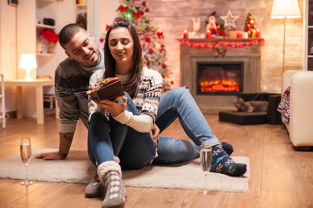 Feliz novia sobre su regalo de Navidad de su novio frente a la cálida chimenea.