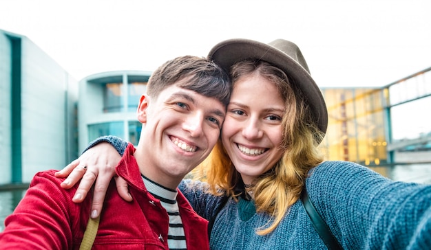 Feliz novio y novia enamorados divirtiéndose genuinamente tomando selfie en el área moderna de Berlín