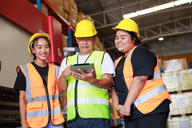 Feliz obesa asiática trabajadora y gerente senior de almacén con chaleco de seguridad y casco duro