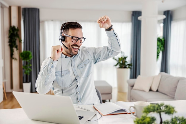 Un feliz operador de soporte técnico trabajando desde casa Un hombre se ríe y celebra el éxito