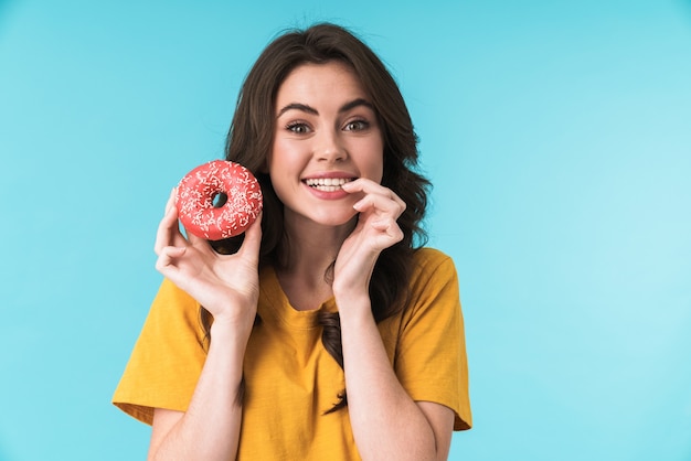 feliz otimista positiva bonita jovem posando isolado sobre a parede azul segurando donut.