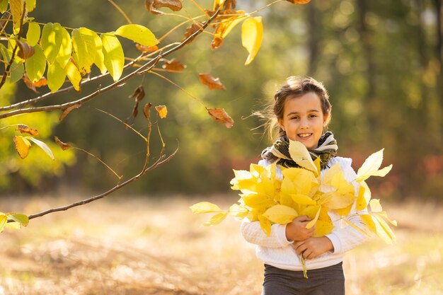 ¡Feliz otoño! Dulce niña jugando con hojas en un parque de otoño. Copie el espacio, hojas caídas.