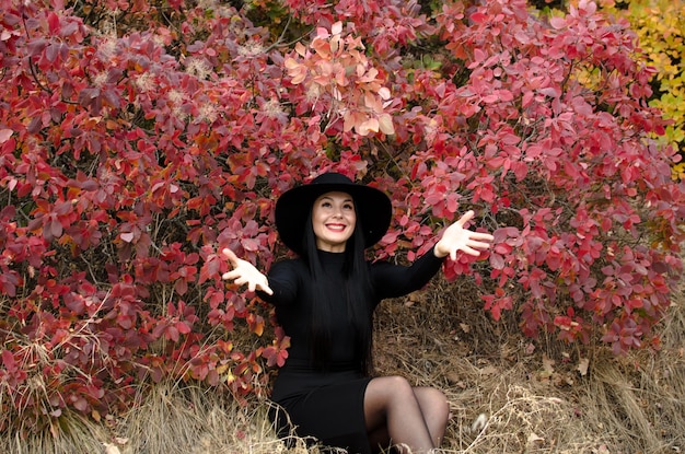 Feliz otoño Hermosa mujer morena sentada en un parque de otoño con un sombrero negro