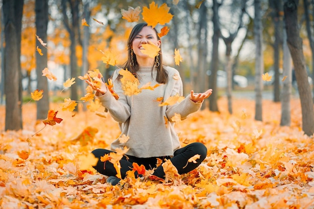 Feliz otoño joven sonriente alegre arroja hojas de otoño afuera en el bosque de otoño raza mixta caucásica mujer de Asia Central