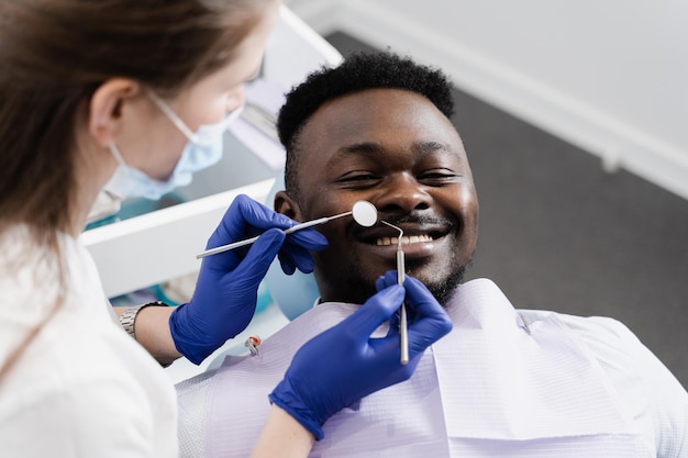 Feliz paciente afroamericano de odontología Tratamiento de dientes Guapo hombre africano sentado en el consultorio dental y sonriente Dentista visitando y consultando