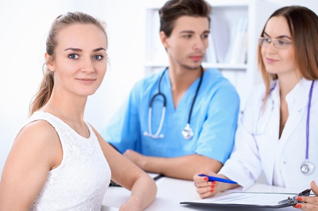 Feliz paciente loira ao lado de alguns médicos no hospital sentados à mesa.